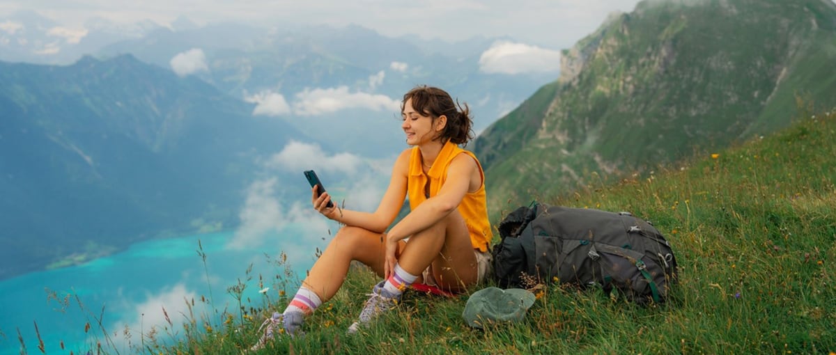donna con cellulare su un prato in montagna