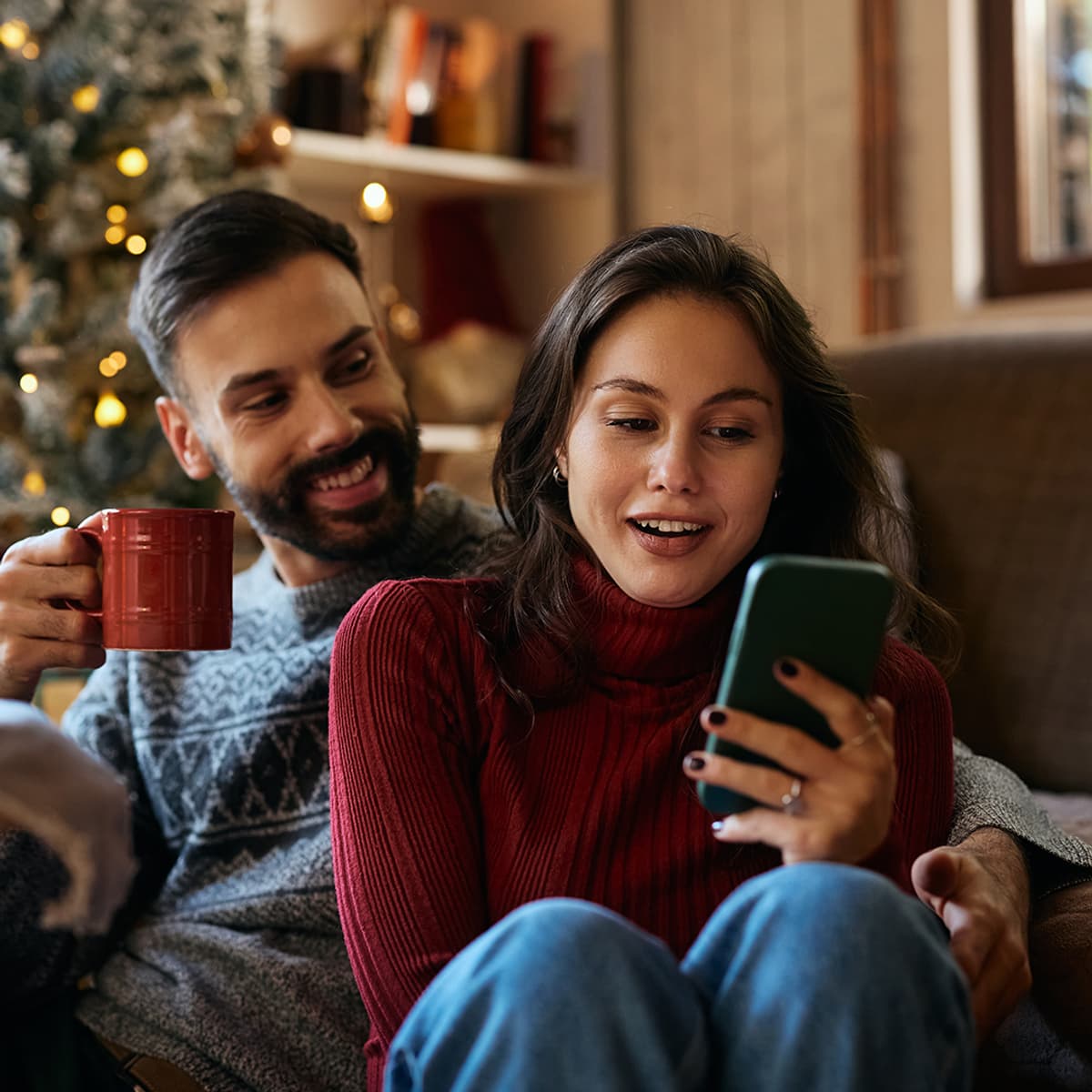 Une femme est assise sur le canapé avec un mec et son téléphone mobile, et elle sourit.