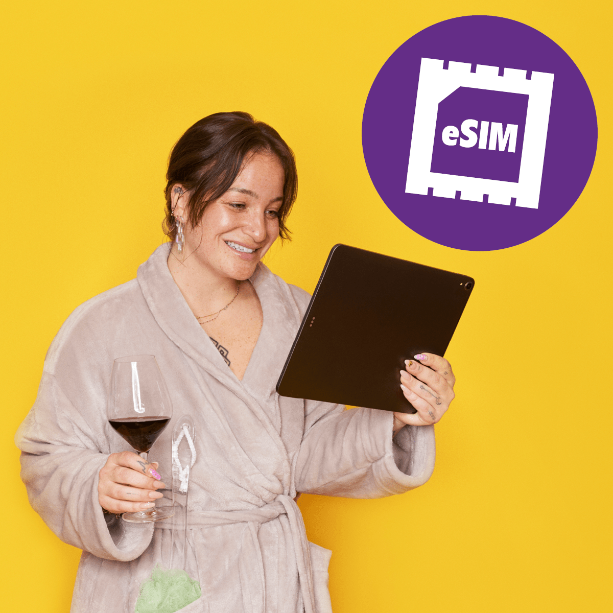Frau in Bademantel mit Tablet und Weinglas in der Hand. eSIM-Logo im Hintergrund.